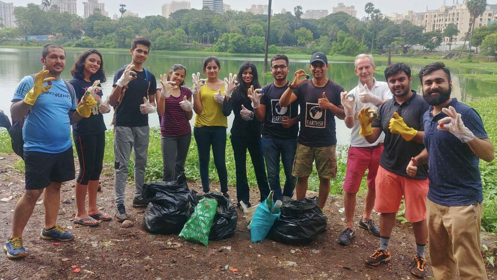 Students and mentors at Powai Lake, Mumbai, holding plastic caps collected from the lake beside bags of collected plastic